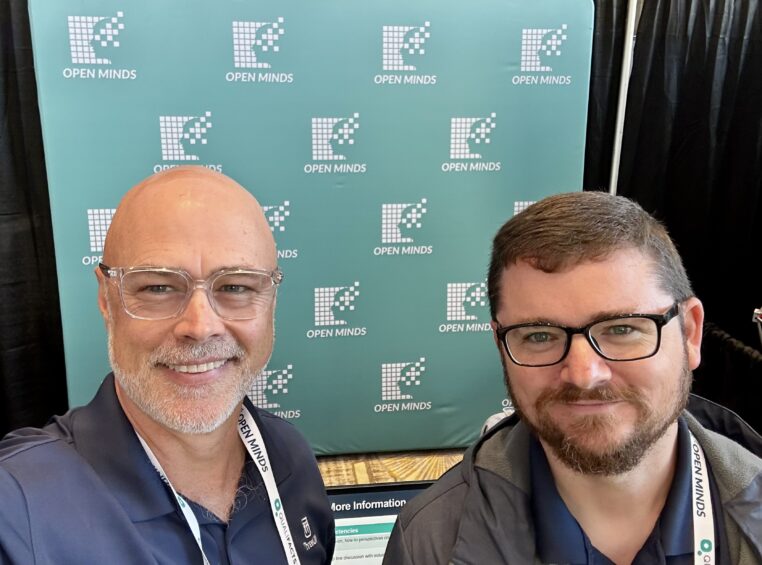 Will Holland and Tommy Ryan standing in front of the OPEN MINDS Technology & Analytics Institute display, 2025