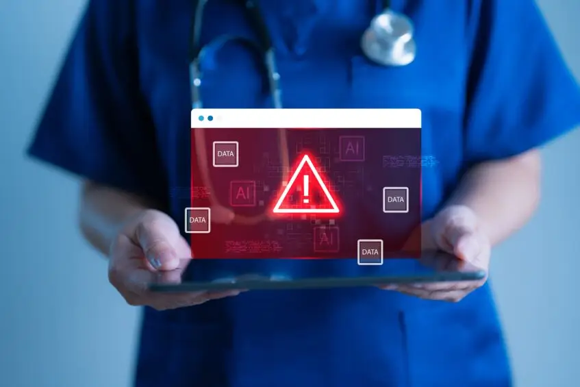 Healthcare professional holding a tablet displaying a red warning symbol over digital data, representing hidden compliance risks in Microsoft 365 environments