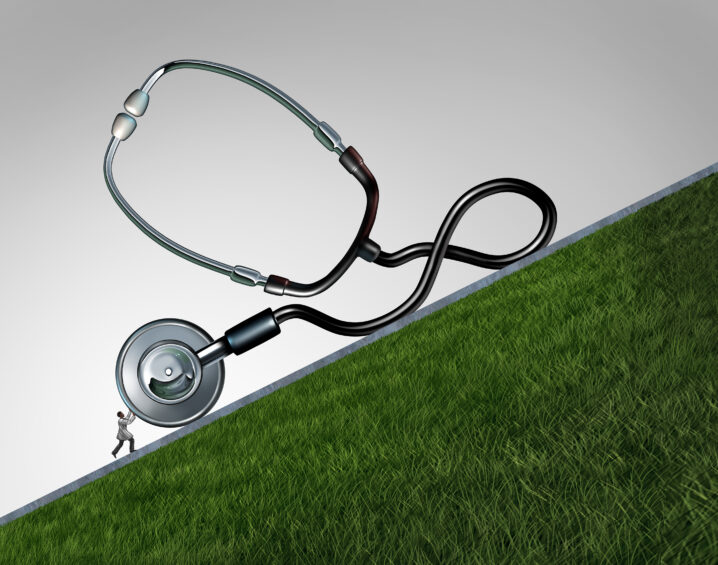 A stethoscope shaped like a large, heavy object being pushed uphill by a small person, symbolizing the challenge of carrying operational or process burdens and the strain caused by poorly defined or inefficient systems.