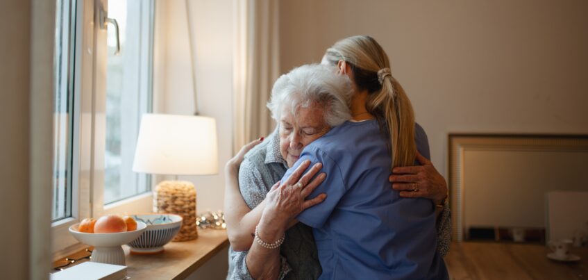 A caregiver and older adult share an embrace, symbolizing the human connection technology should protect, not replace.